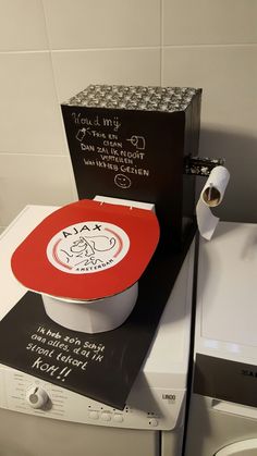 a red and white bowl sitting on top of a dryer next to a roll of toilet paper