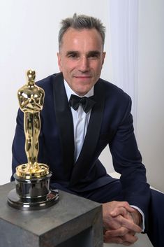 a man in a tuxedo sitting next to an oscar statue