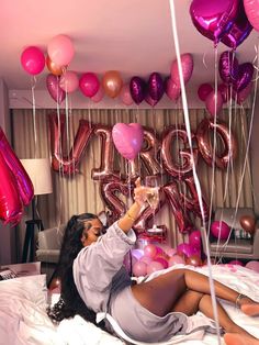 a woman laying on top of a bed surrounded by pink and purple balloons with the word love spelled in large letters