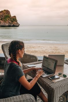 a woman sitting at a table on top of a laptop computer next to the ocean