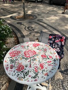 a table and chair sitting on the sidewalk in front of a tree with flowers painted on it