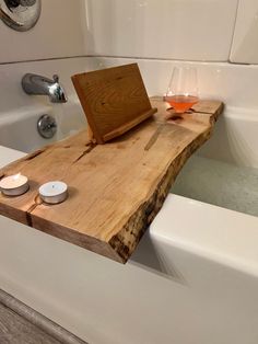 a bath tub with a wooden tray and two candles on it next to a glass of wine