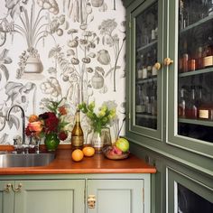 a kitchen with green cabinets and floral wallpaper on the walls, along with various fruits and vegetables