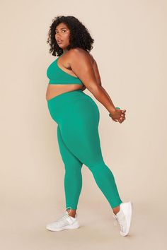 a woman in green leggings and white sneakers is posing with her hands on her hips