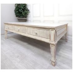 an old white coffee table with drawers on the bottom, and a potted plant behind it