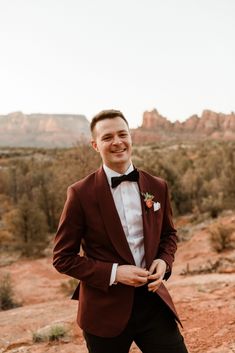 a man in a suit and bow tie posing for the camera with mountains in the background