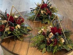 three gold triangles with flowers and greenery in them on a wooden table, surrounded by wood flooring