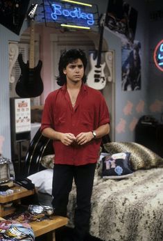 the young man is standing in front of his bed with guitars hanging on the wall