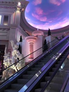 an escalator in a shopping mall with statues on the bottom and sky above