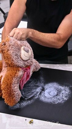 a man holding a teddy bear on top of a piece of paper in front of him