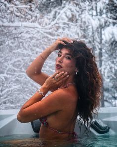 a woman in a hot tub with snow on the ground and trees behind her, looking off into the distance