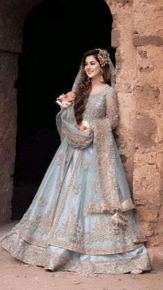 a woman in a blue wedding dress standing by a stone wall