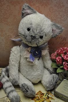 a white stuffed cat sitting on top of a table next to pink flowers and a book