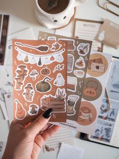 a person holding up some stickers on top of a white table next to a cup of coffee