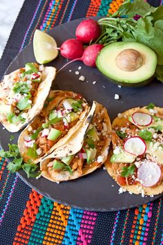 three tacos on a plate with avocado and radishes