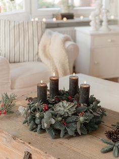 a christmas wreath with candles and greenery on a coffee table