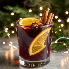 a drink with orange slices and cinnamon sticks in it on a table next to christmas lights