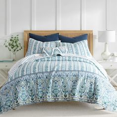 a bed with blue and white bedspread on top of it next to a night stand