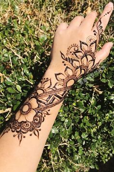 a henna tattoo on someone's hand with green grass and bushes in the background