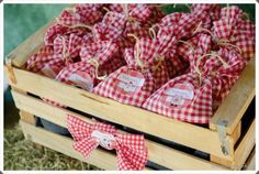 red and white gingham bags sitting in a wooden crate on some hay with twine bows tied around them