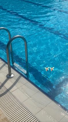 an empty swimming pool with blue water and metal handrails in the foreground