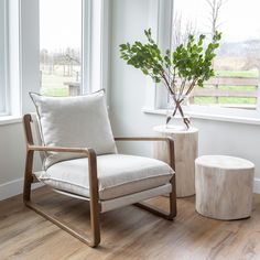 a white chair sitting in front of a window next to a wooden table with a potted plant on it