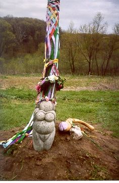 a stone sculpture with ribbons on it in the middle of a grassy area next to trees