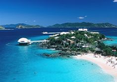 an island in the middle of blue water with white sand and palm trees on it