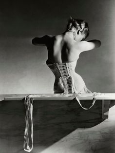 an old photo of a woman in corses sitting on a table with her hands behind her back