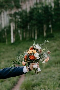 a man holding a bouquet of flowers in his hand while walking down a path through the woods