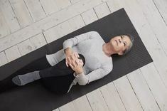 an older woman sitting on a yoga mat holding her hands together