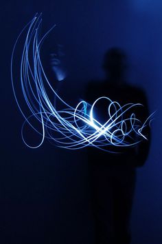 a man standing in front of a blue wall holding a cell phone with light painting on it