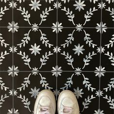 a pair of white shoes standing in front of a black and white tile wall with flowers on it