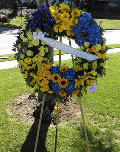 a memorial wreath with flowers and a ribbon on it in the grass near a street