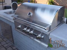 a stainless steel grill with four burners and sink on the outside of a house