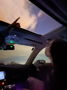 a person driving a car at dusk with the sun going down and clouds in the background