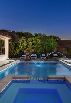 an outdoor swimming pool with lounge chairs and trees in the background at night, lit up by blue lights