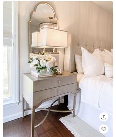 a bedroom with a bed, nightstand and flowers on the table in front of it