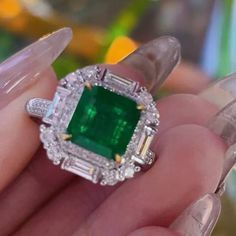 a close up of a person holding an emerald and diamond ring