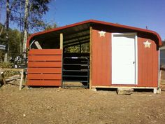 a red shed with white doors and stars painted on the side, sitting in dirt area next to trees