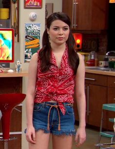 the young woman is standing in her kitchen wearing short shorts and a red shirt with paisley print on it