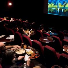 people are sitting in the movie theater and eating their meals on trays while watching television