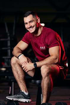 a man sitting on top of a black stool next to a pair of dumbbells