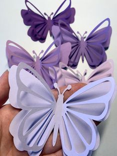 hand holding purple and white paper butterflies in front of the camera, with another butterfly behind it