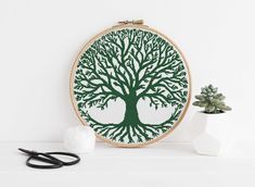 a cross - stitch tree with green leaves and branches on it, next to some scissors