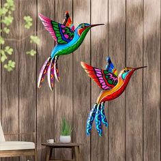 two colorful hummingbirds are flying over a wooden fence, one is painted multicolored