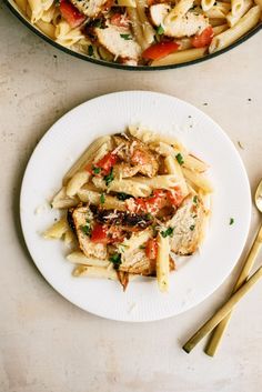 pasta with chicken, tomatoes and parmesan cheese on a plate next to a skillet