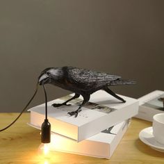 a black bird sitting on top of a stack of books next to a cup and saucer