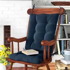 a rocking chair in front of a fireplace with books on the mantle and flowers beside it