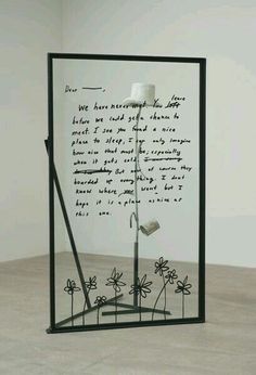 a piece of art with writing on it in front of a glass frame that is sitting on the floor